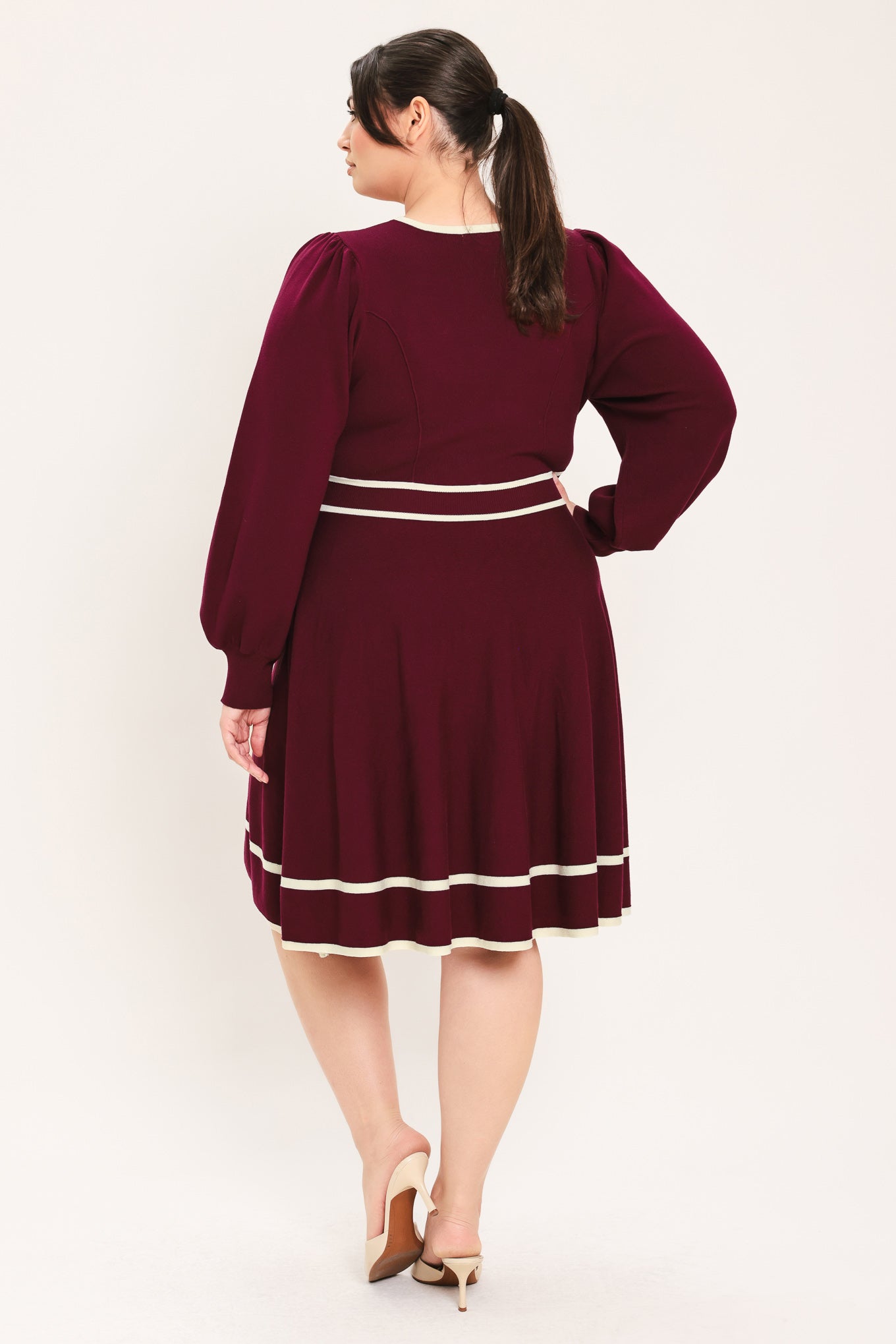 A woman wearing a long-sleeve skater dress in deep wine with cream stripe accents at the waist and hem | Flying Tomato Curve