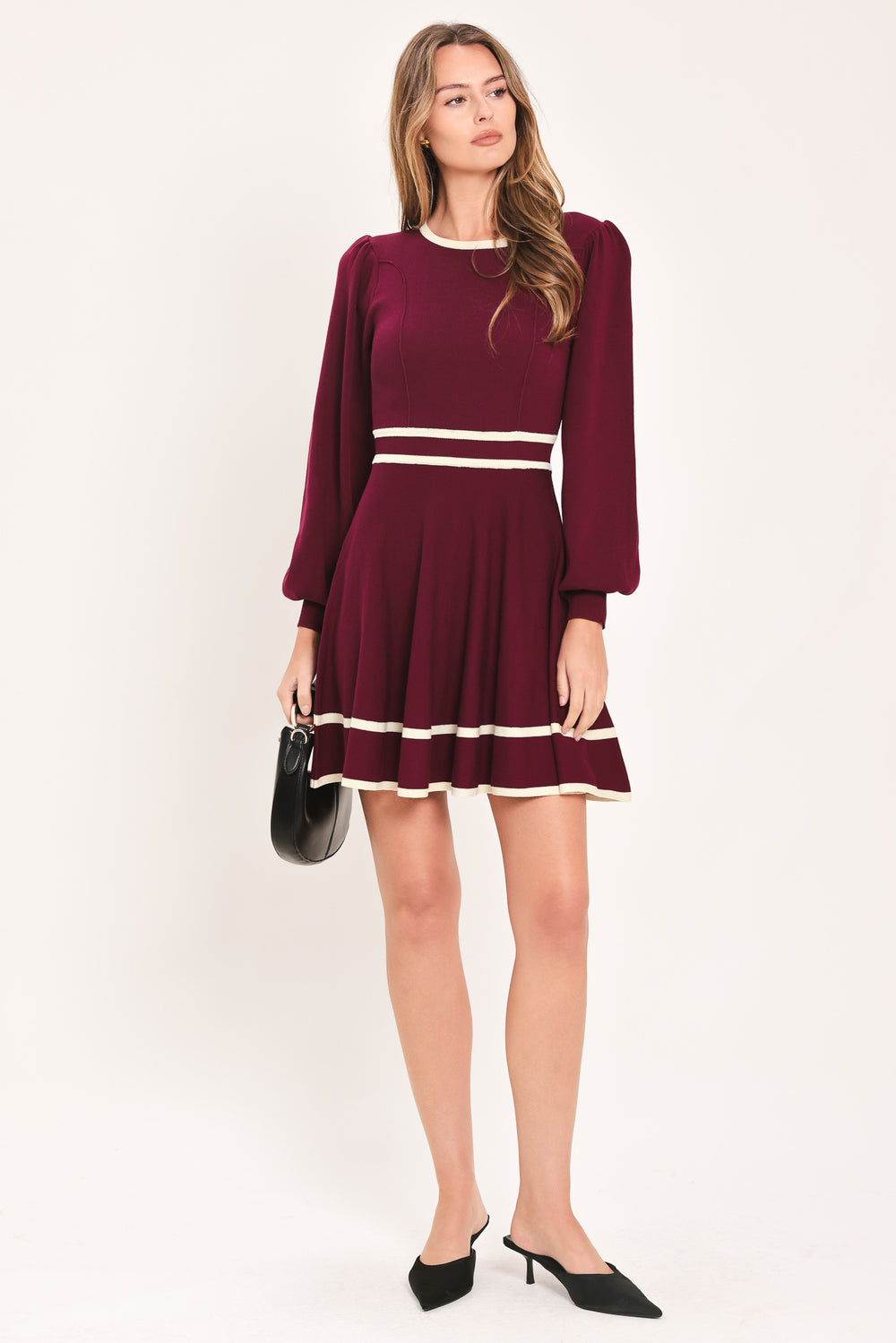 A woman wearing a long-sleeve skater dress in deep wine with cream stripe accents at the waist and hem | Flying Tomato