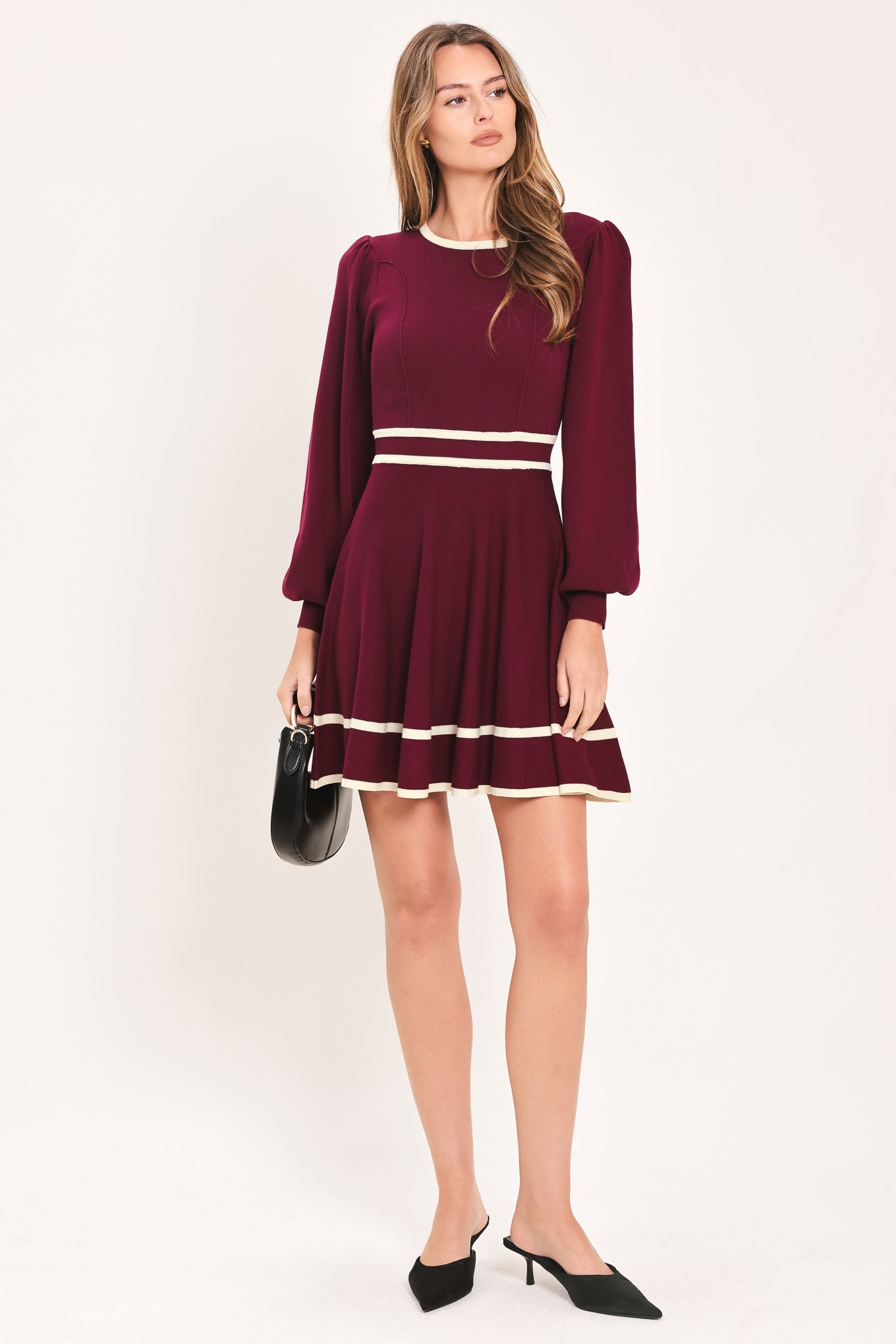 A woman wearing a long-sleeve skater dress in deep wine with cream stripe accents at the waist and hem | Flying Tomato