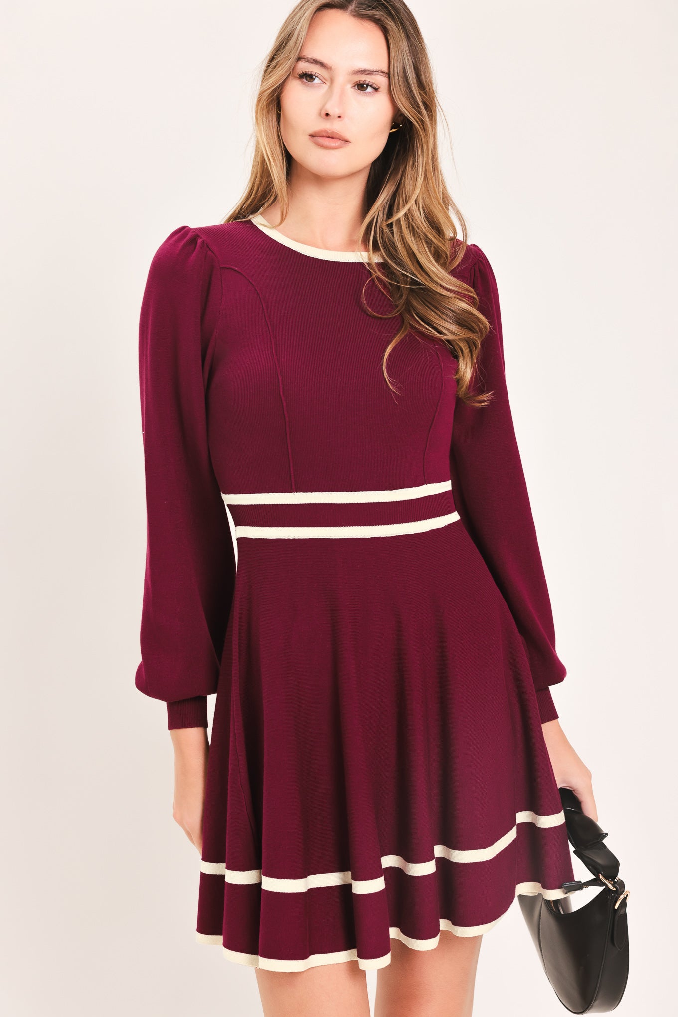 A woman wearing a long-sleeve skater dress in deep wine with cream stripe accents at the waist and hem | Flying Tomato