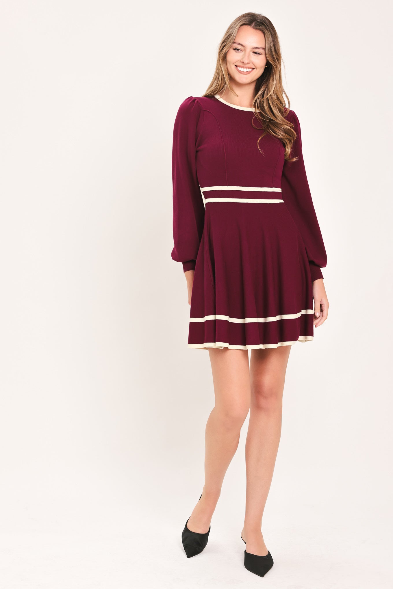 A woman wearing a long-sleeve skater dress in deep wine with cream stripe accents at the waist and hem | Flying Tomato