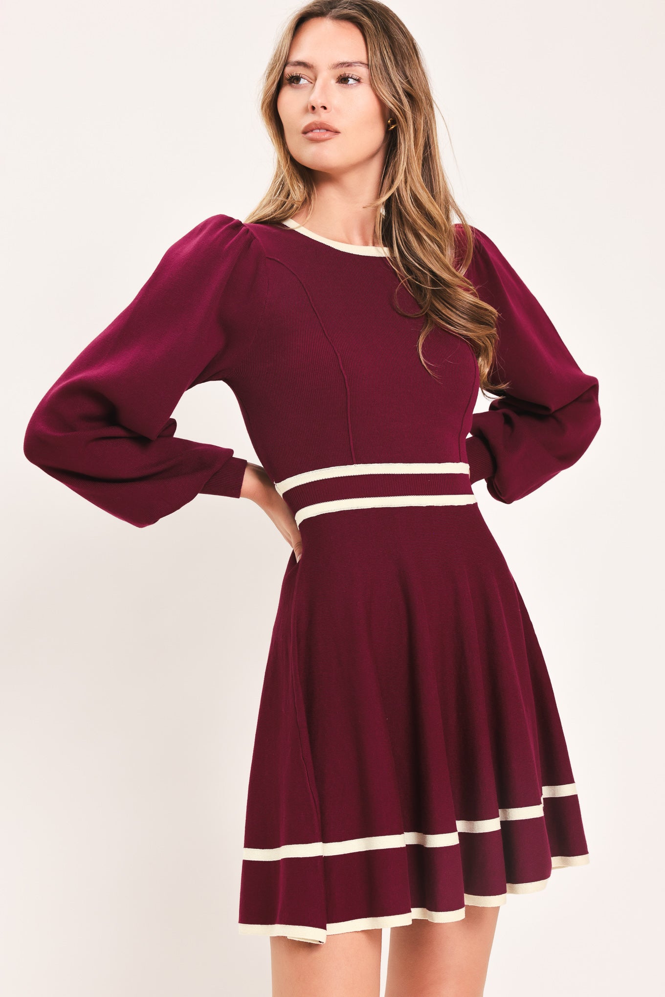 A woman wearing a long-sleeve skater dress in deep wine with cream stripe accents at the waist and hem | Flying Tomato