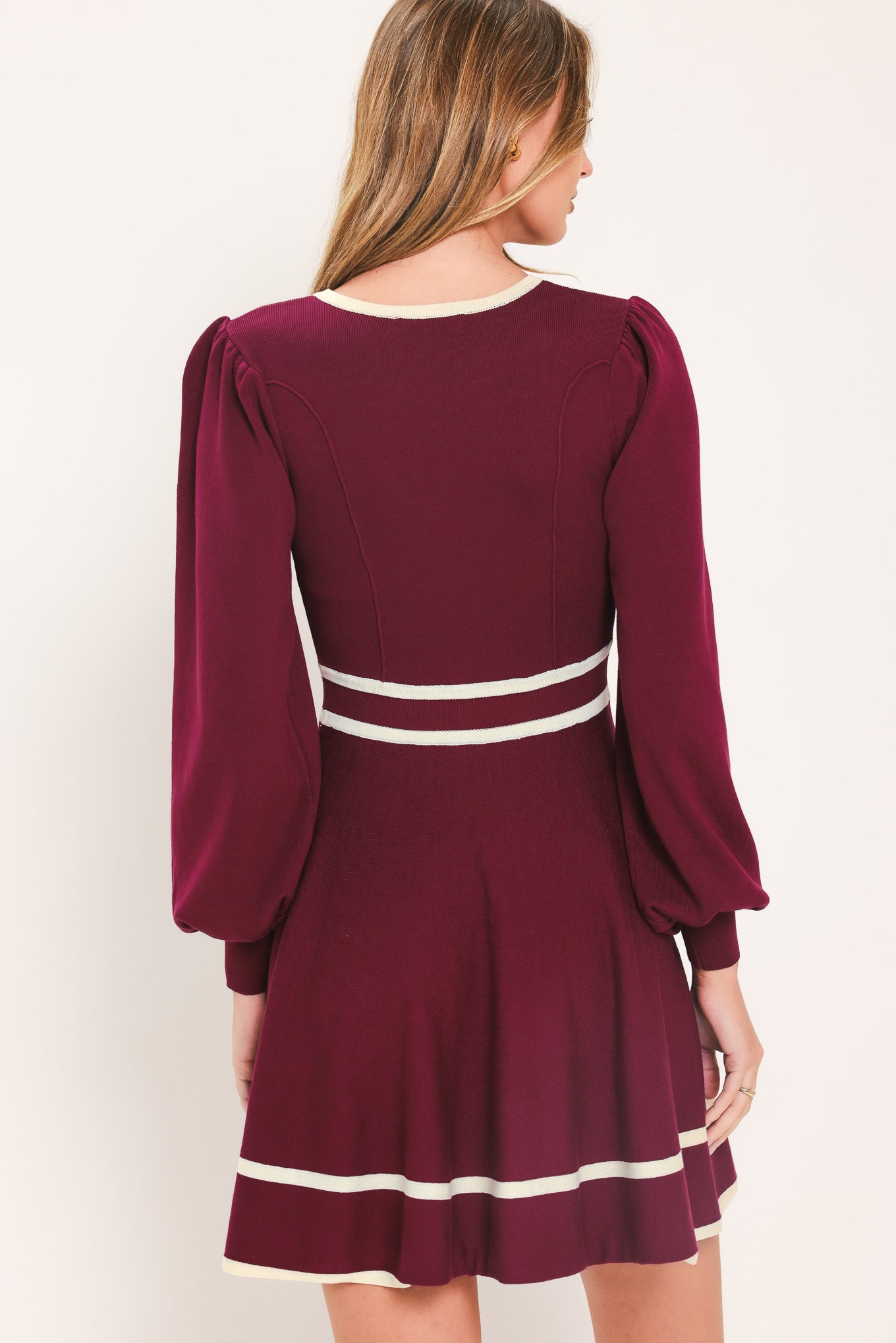 A woman wearing a long-sleeve skater dress in deep wine with cream stripe accents at the waist and hem | Flying Tomato