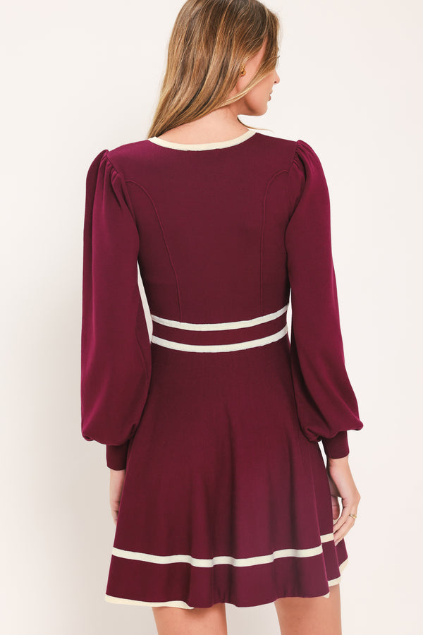 A woman wearing a long-sleeve skater dress in deep wine with cream stripe accents at the waist and hem | Flying Tomato