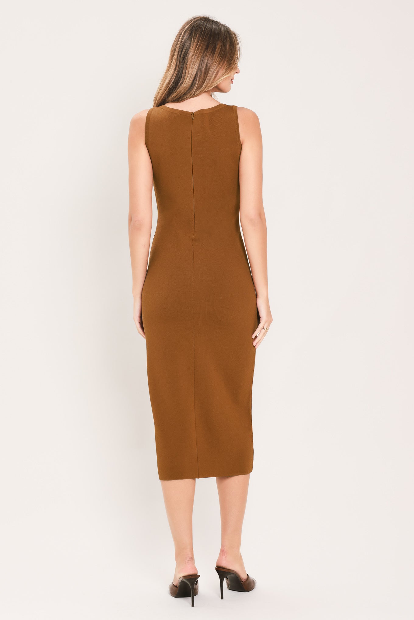 A woman wearing a sleeveless, high-neck, sweater knot bodycon midi dress in a warm camel brown color | Flying Tomato