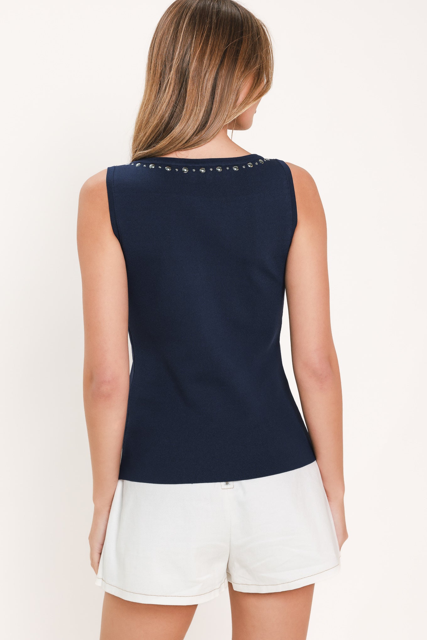 Woman wearing a navy blue sleeveless sweater knit top with a high neck and studded details along the neckline and armholes | Flying Tomato