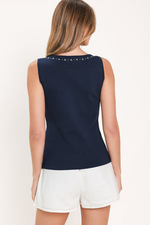 Woman wearing a navy blue sleeveless sweater knit top with a high neck and studded details along the neckline and armholes | Flying Tomato