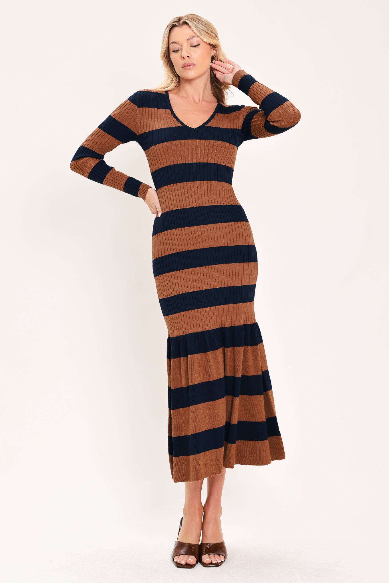 A woman modeling a long-sleeve ribbed knit midi dress with horizontal brown and navy and rust stripes, featuring a V-neckline and a flared mermaid-style hem | Flying Tomato