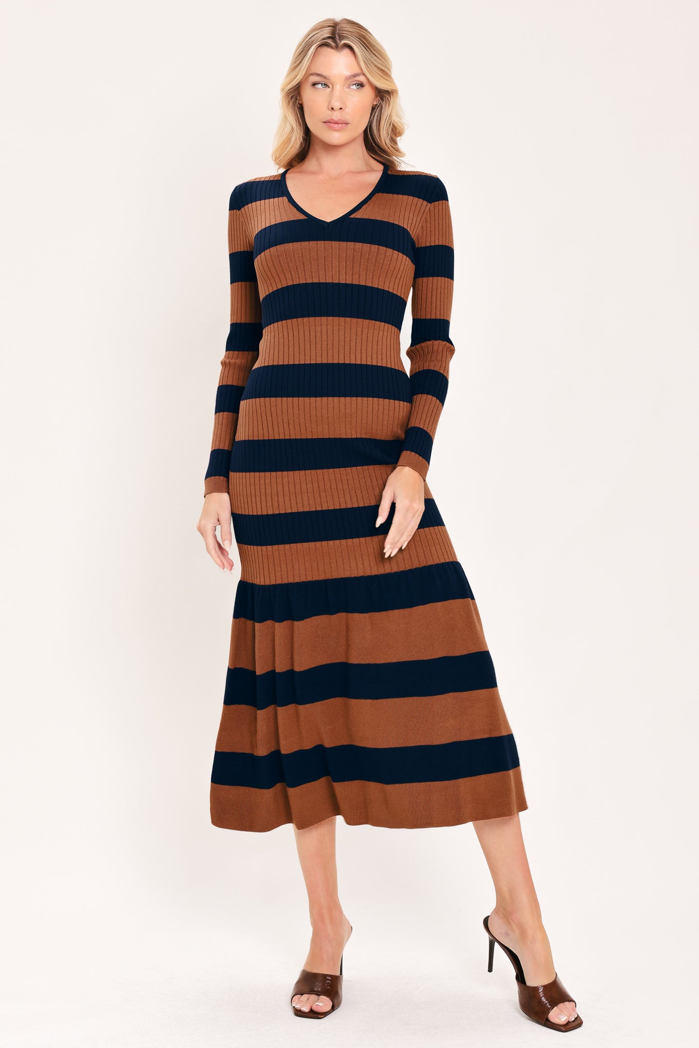 A woman modeling a long-sleeve ribbed knit midi dress with horizontal brown and navy and rust stripes, featuring a V-neckline and a flared mermaid-style hem | Flying Tomato