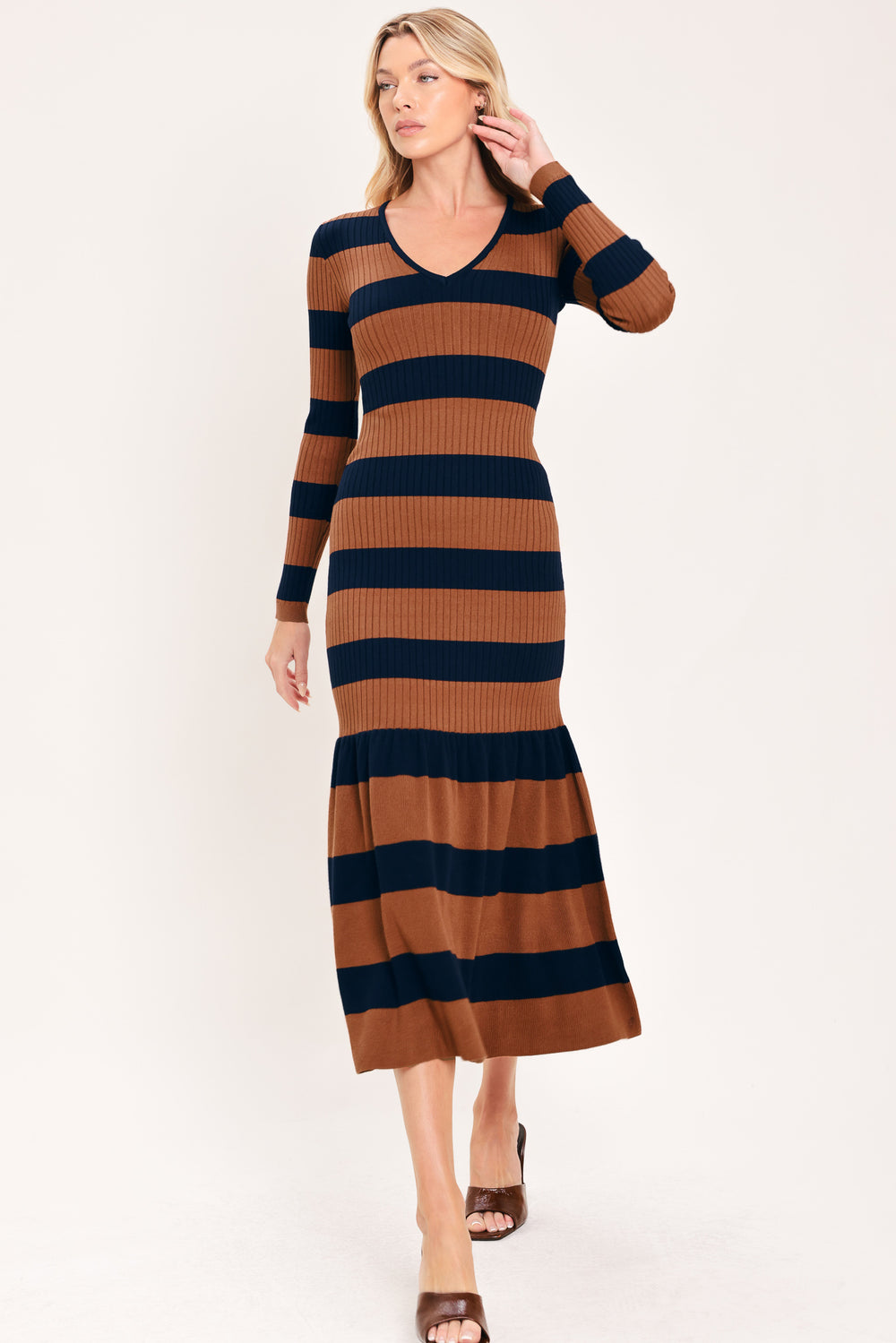 A woman modeling a long-sleeve ribbed knit midi dress with horizontal brown and navy and rust stripes, featuring a V-neckline and a flared mermaid-style hem | Flying Tomato