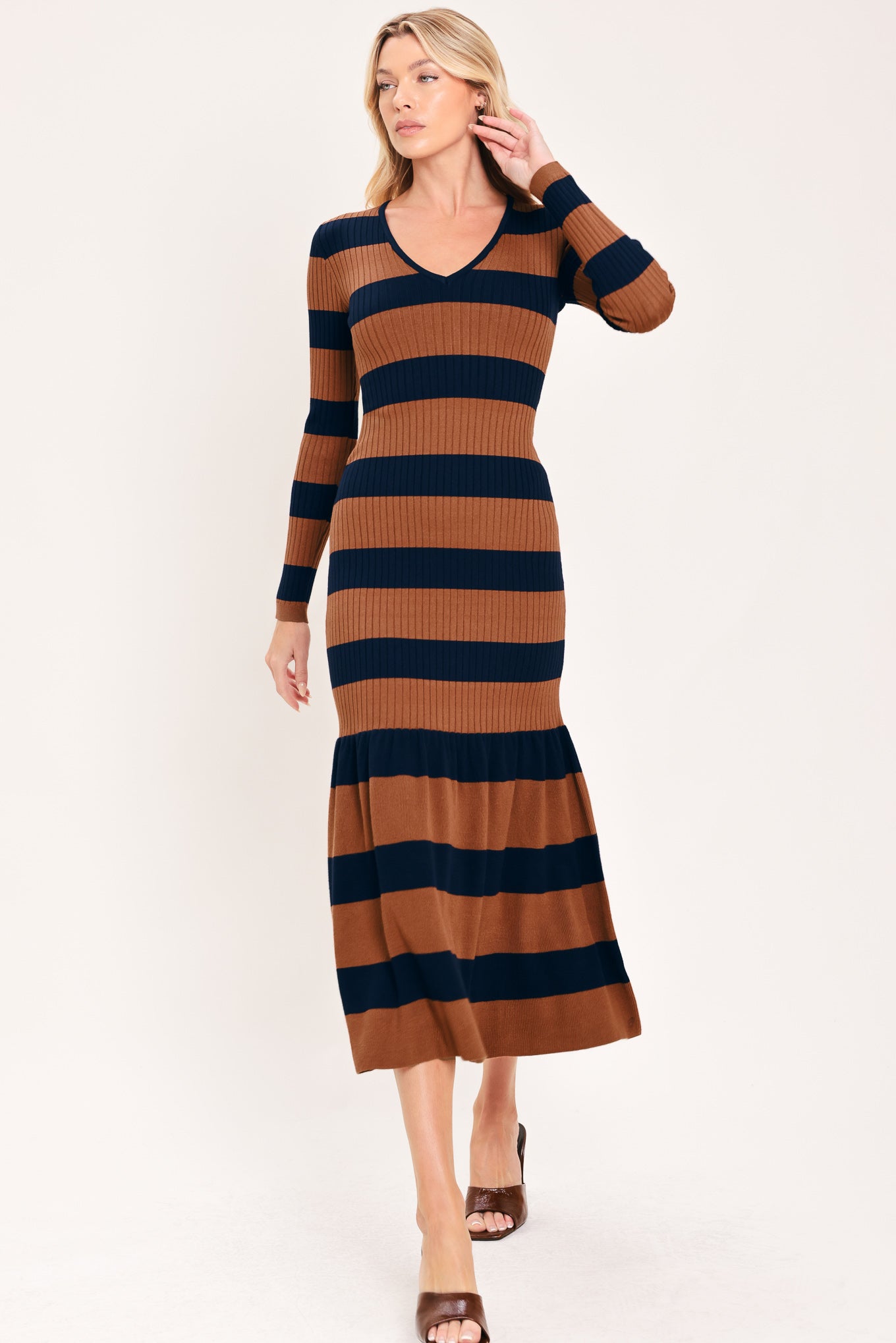 A woman modeling a long-sleeve ribbed knit midi dress with horizontal brown and navy and rust stripes, featuring a V-neckline and a flared mermaid-style hem | Flying Tomato