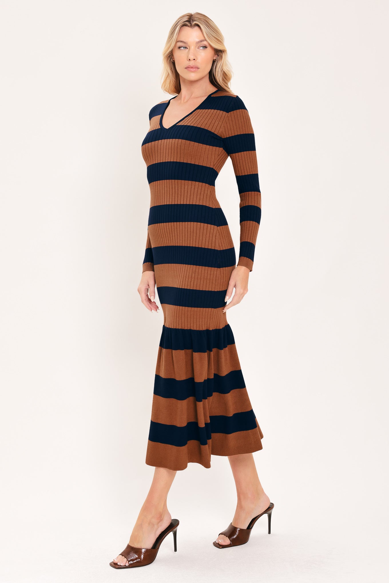A woman modeling a long-sleeve ribbed knit midi dress with horizontal brown and navy and rust stripes, featuring a V-neckline and a flared mermaid-style hem | Flying Tomato