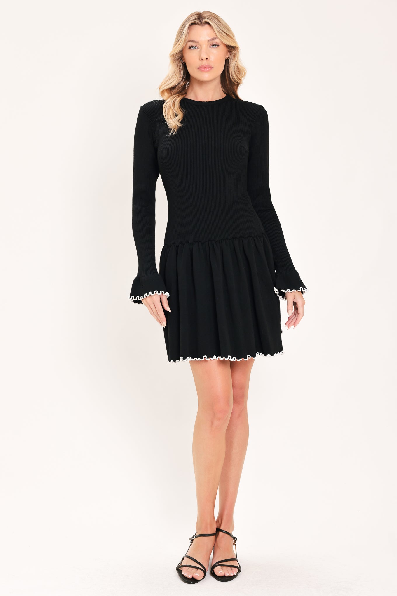 A woman modeling a black long-sleeve ribbed mini dress with white ruffle trim at the cuffs and hem | Flying Tomato