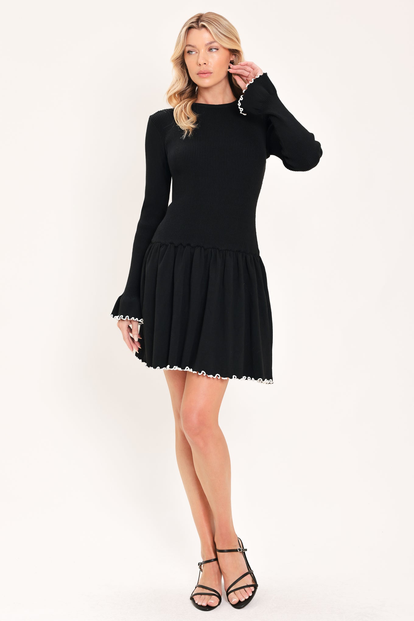 A woman modeling a black long-sleeve ribbed mini dress with white ruffle trim at the cuffs and hem | Flying Tomato