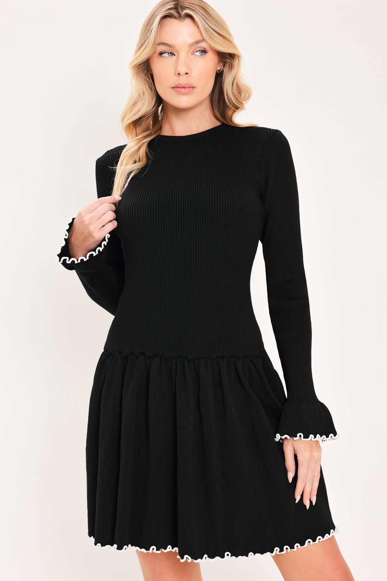 A woman modeling a black long-sleeve ribbed mini dress with white ruffle trim at the cuffs and hem | Flying Tomato
