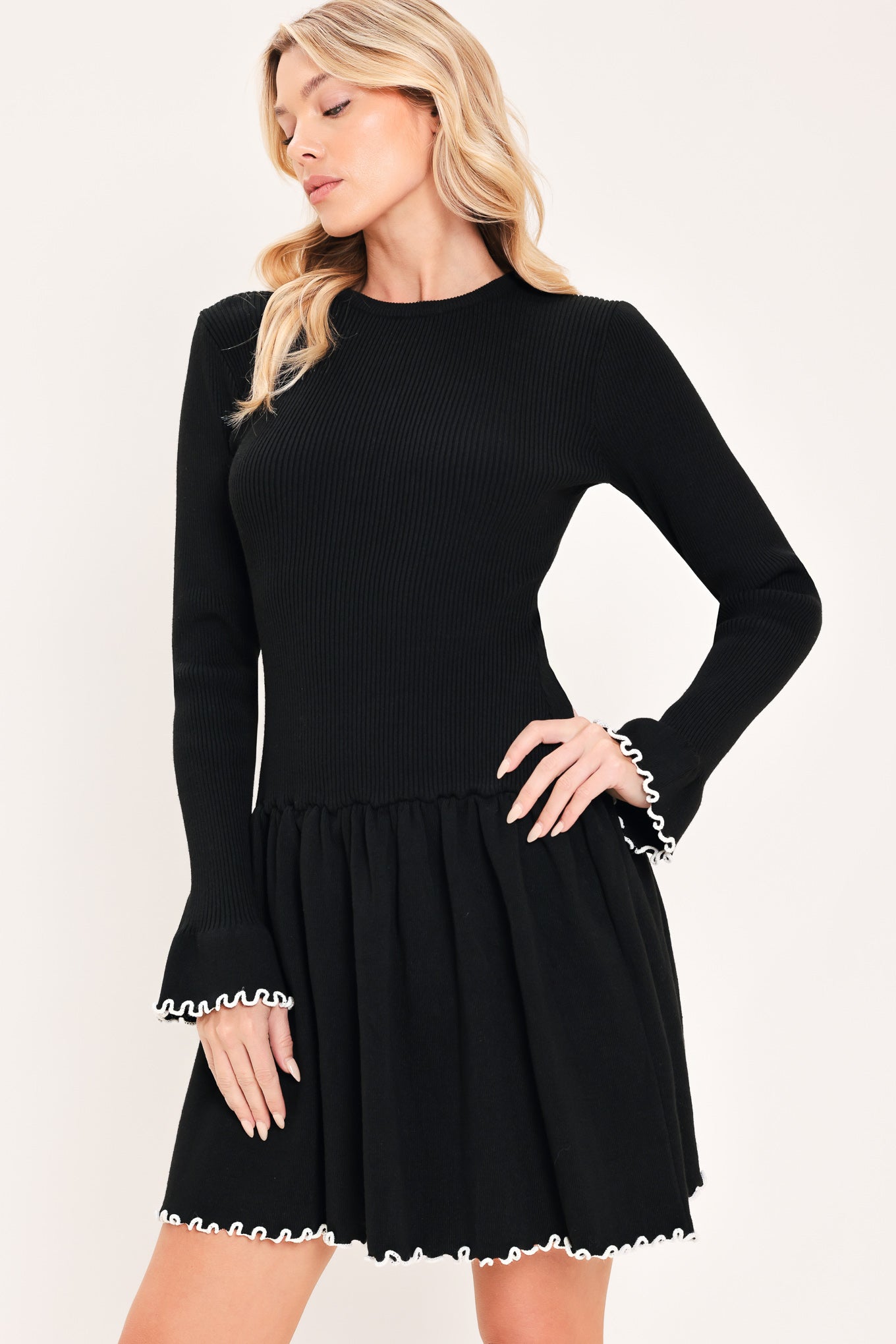 A woman modeling a black long-sleeve ribbed mini dress with white ruffle trim at the cuffs and hem | Flying Tomato