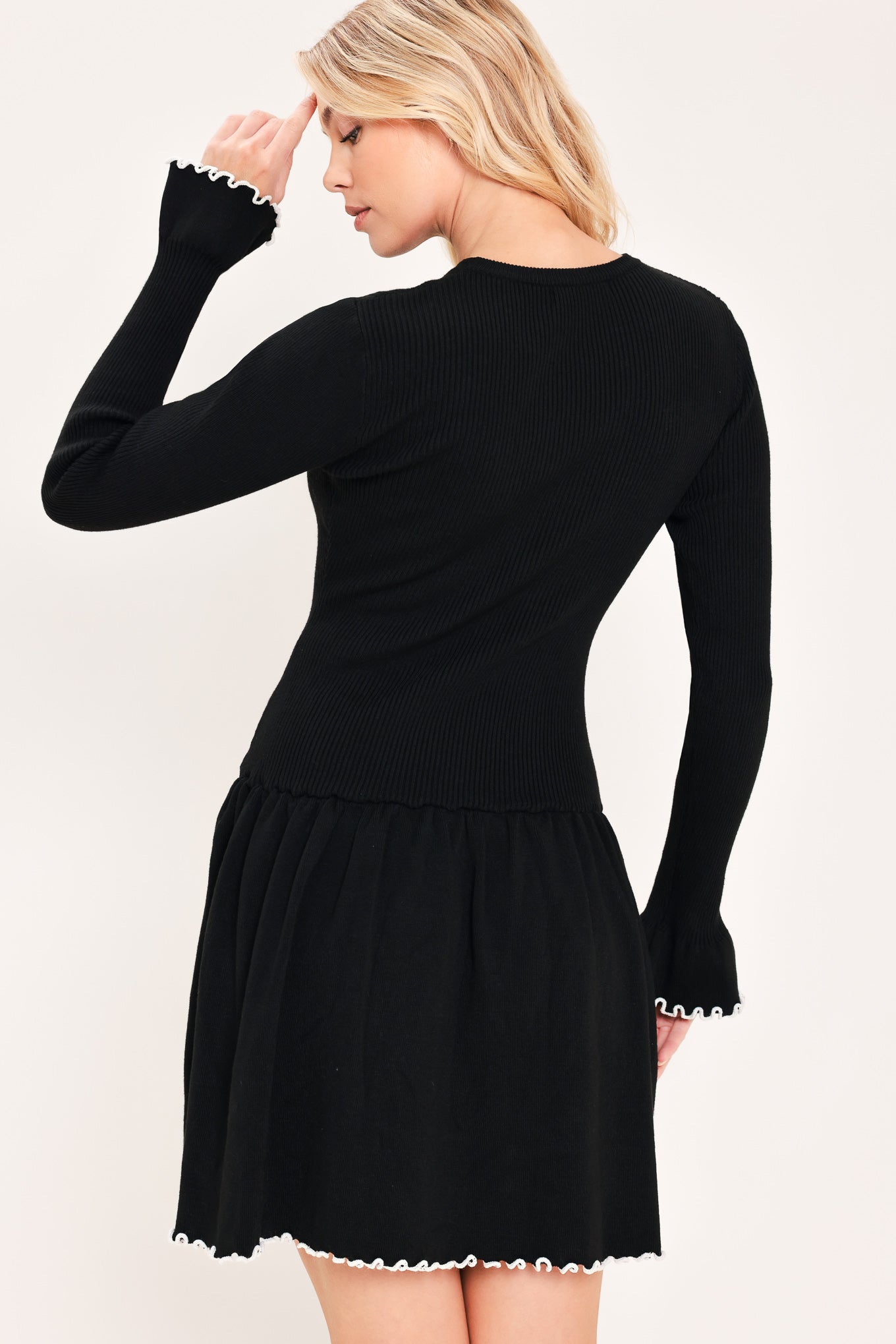 A woman modeling a black long-sleeve ribbed mini dress with white ruffle trim at the cuffs and hem | Flying Tomato