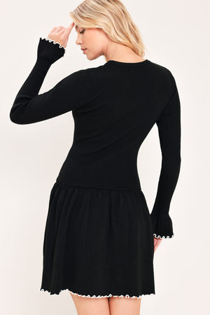 A woman modeling a black long-sleeve ribbed mini dress with white ruffle trim at the cuffs and hem | Flying Tomato