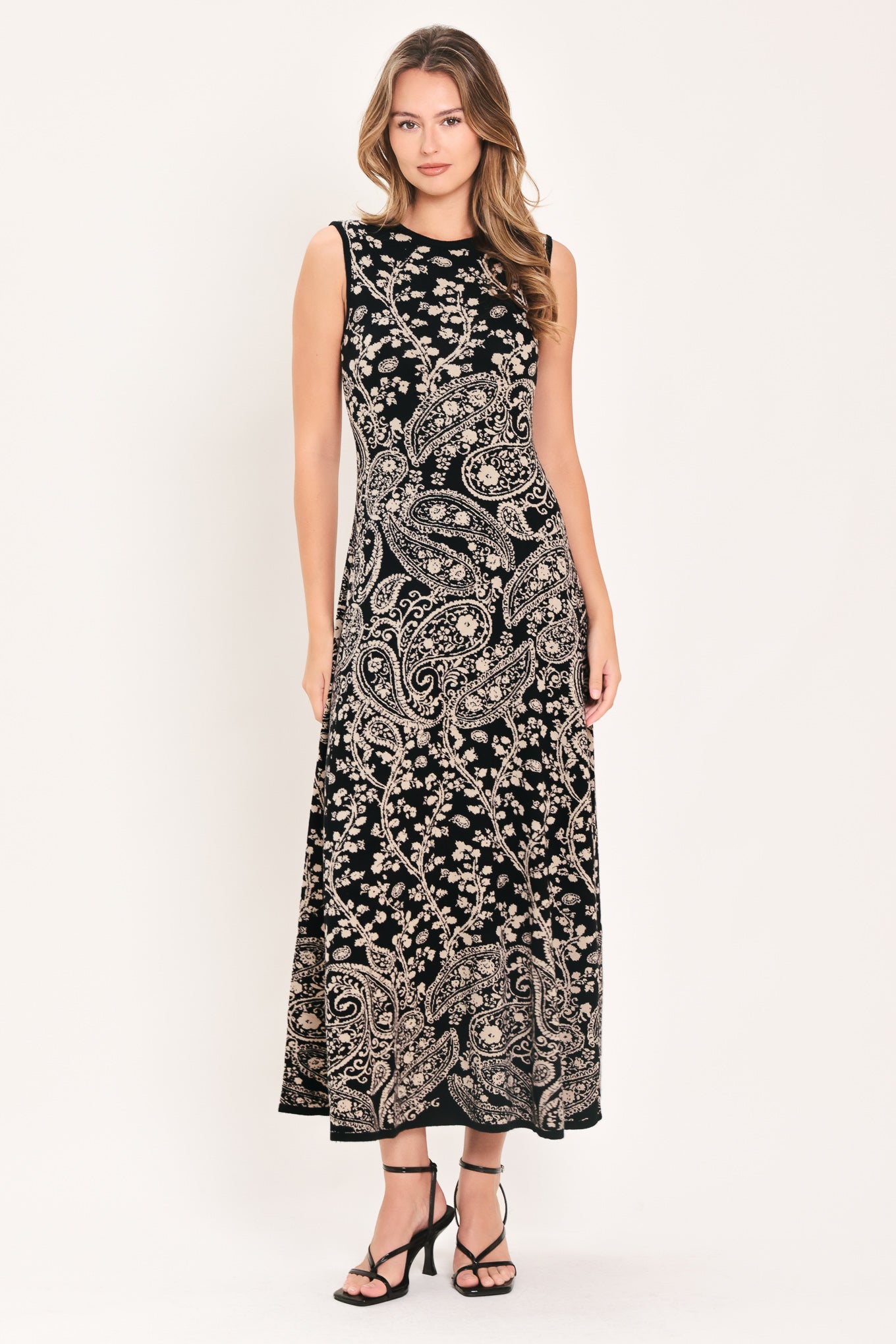 A woman wearing a sleeveless black midi dress with an intricate white paisley and floral pattern | Flying Tomato