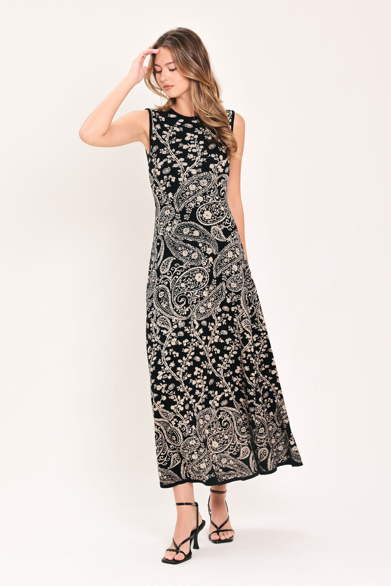 A woman wearing a sleeveless black midi dress with an intricate white paisley and floral pattern | Flying Tomato