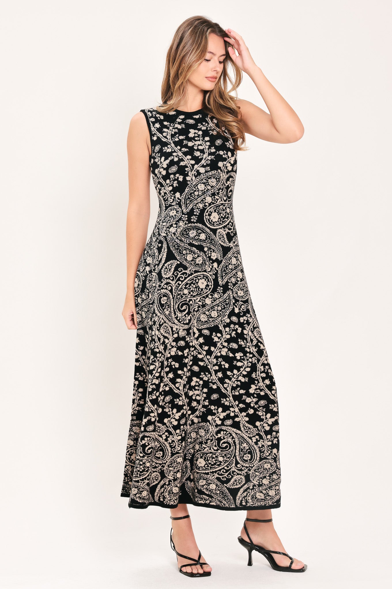 A woman wearing a sleeveless black midi dress with an intricate white paisley and floral pattern | Flying Tomato
