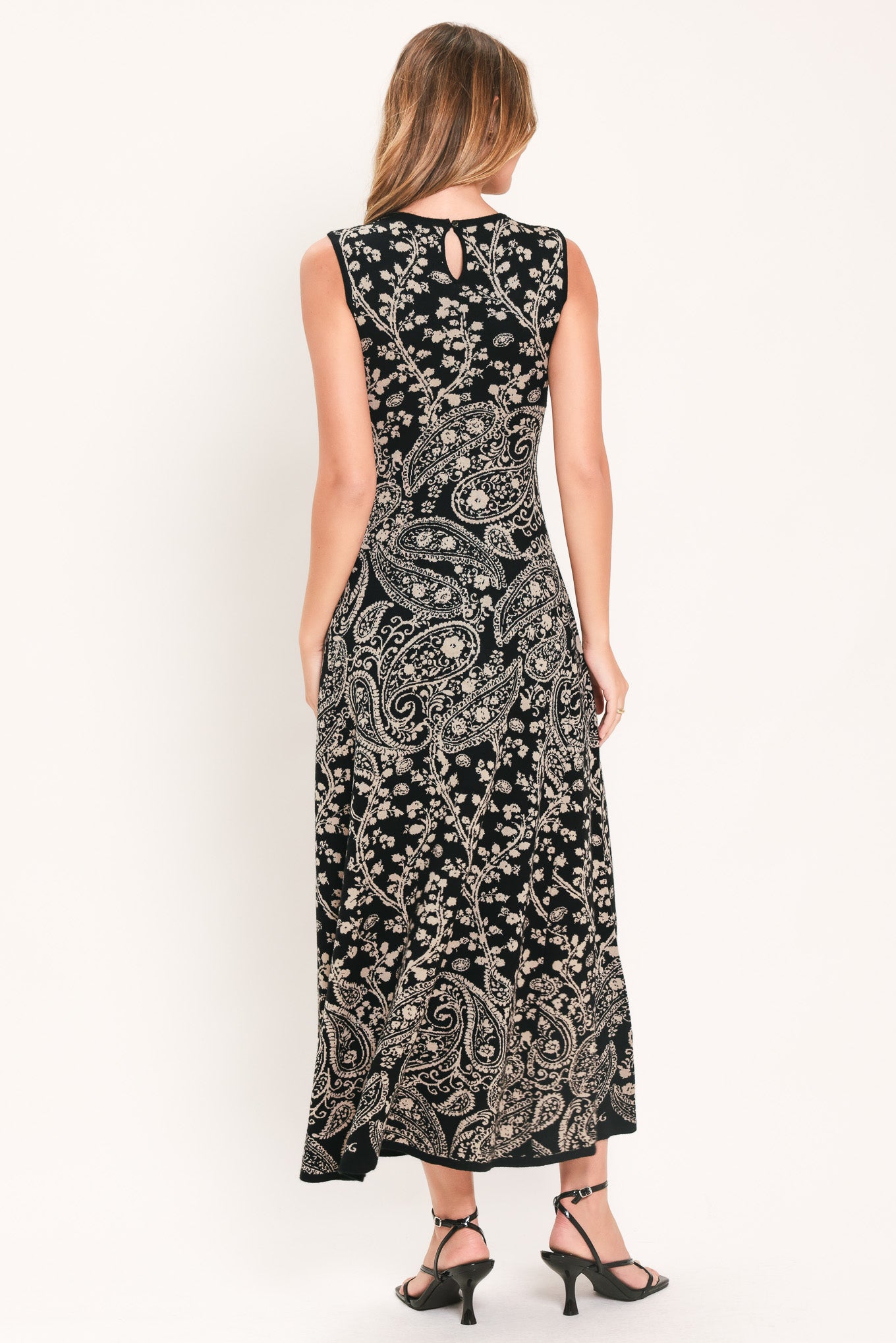 A woman wearing a sleeveless black midi dress with an intricate white paisley and floral pattern | Flying Tomato