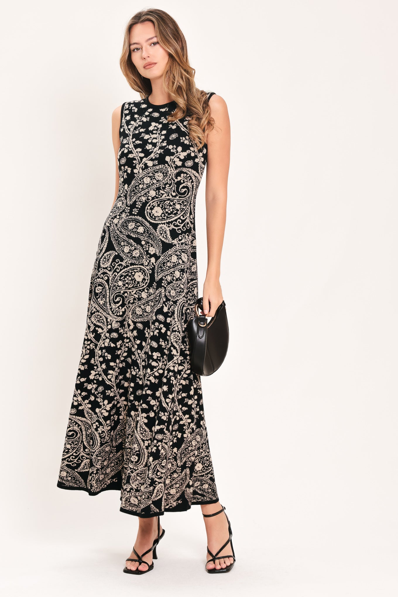 A woman wearing a sleeveless black midi dress with an intricate white paisley and floral pattern | Flying Tomato