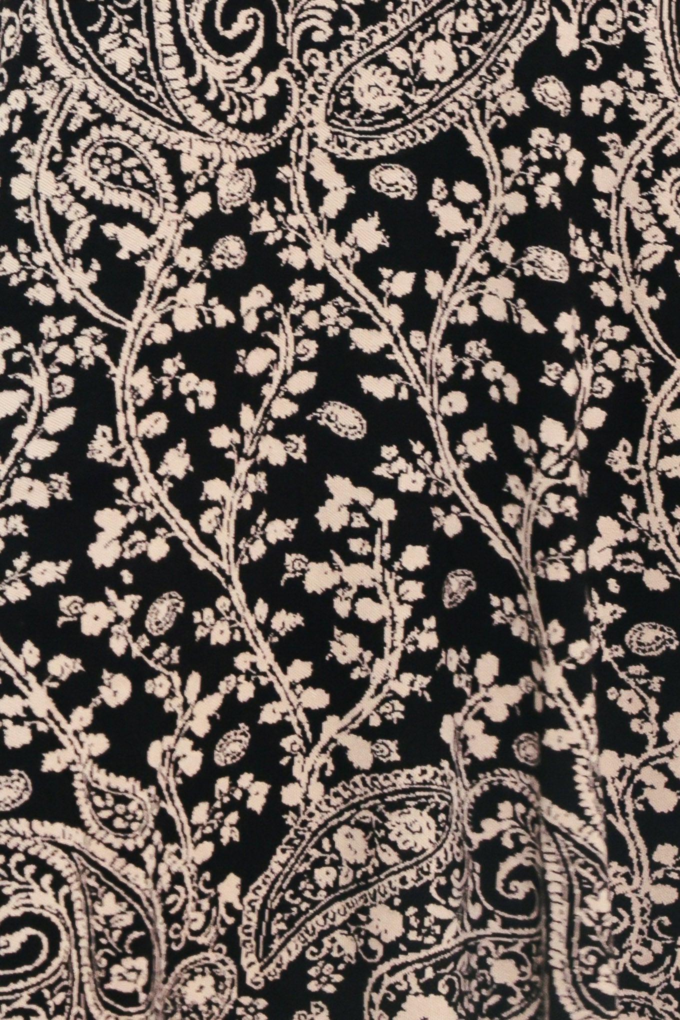 A woman wearing a sleeveless black midi dress with an intricate white paisley and floral pattern | Flying Tomato