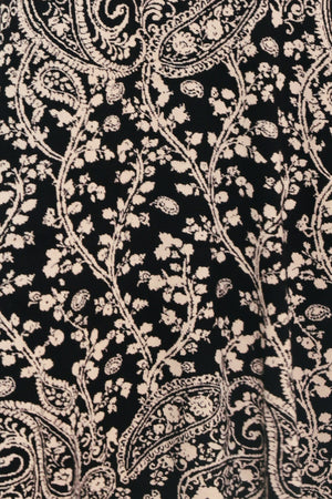 A woman wearing a sleeveless black midi dress with an intricate white paisley and floral pattern | Flying Tomato