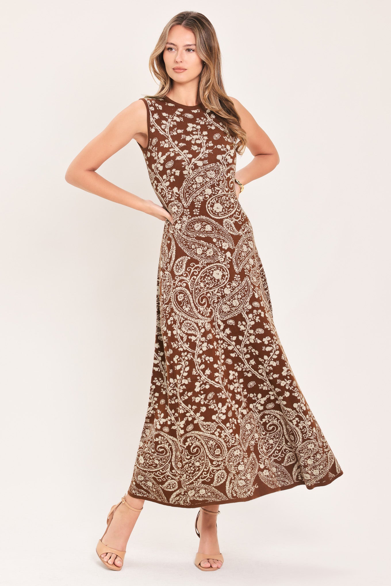 A woman wearing a sleeveless camel midi dress with an intricate white paisley and floral pattern | Flying Tomato