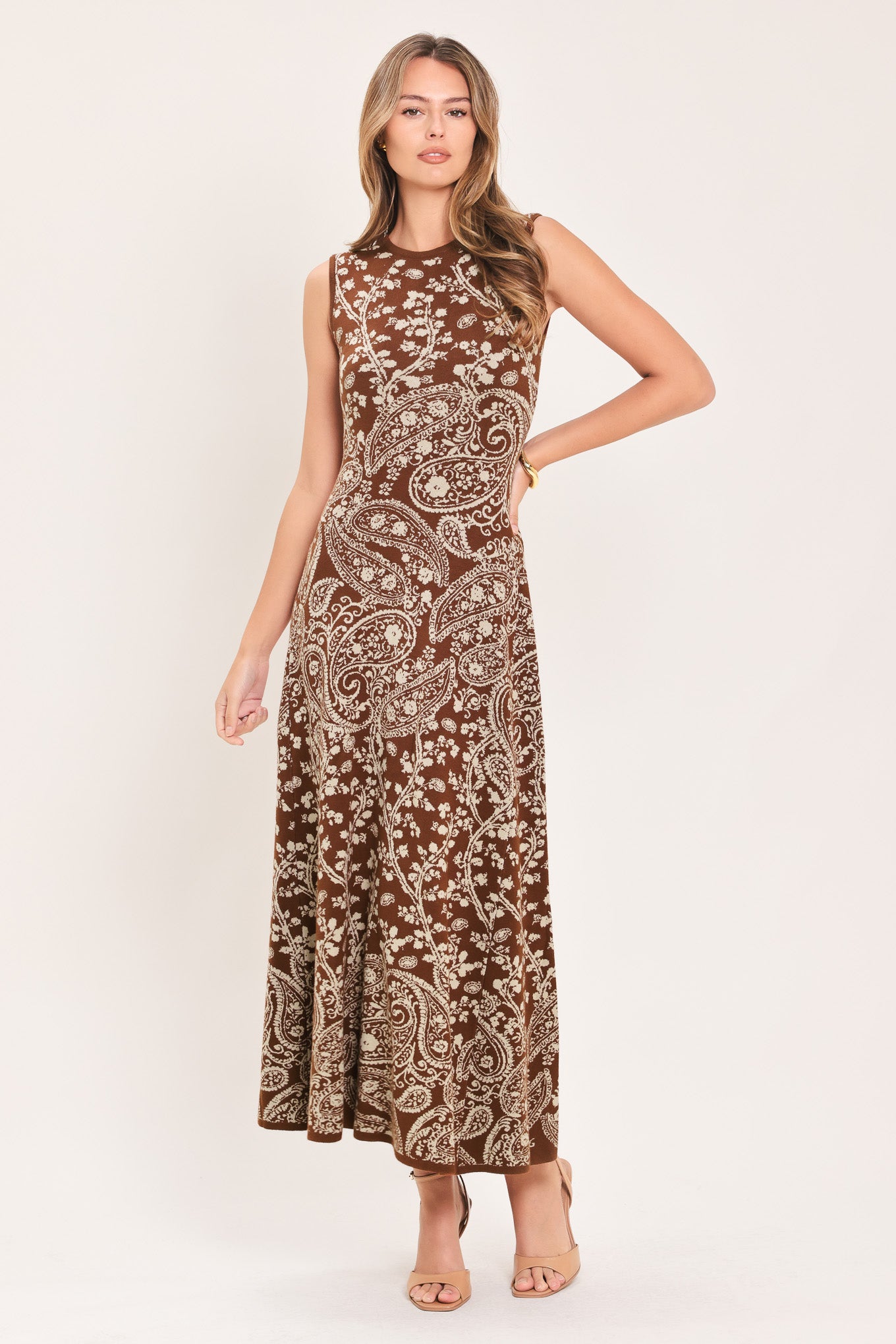 A woman wearing a sleeveless camel midi dress with an intricate white paisley and floral pattern | Flying Tomato