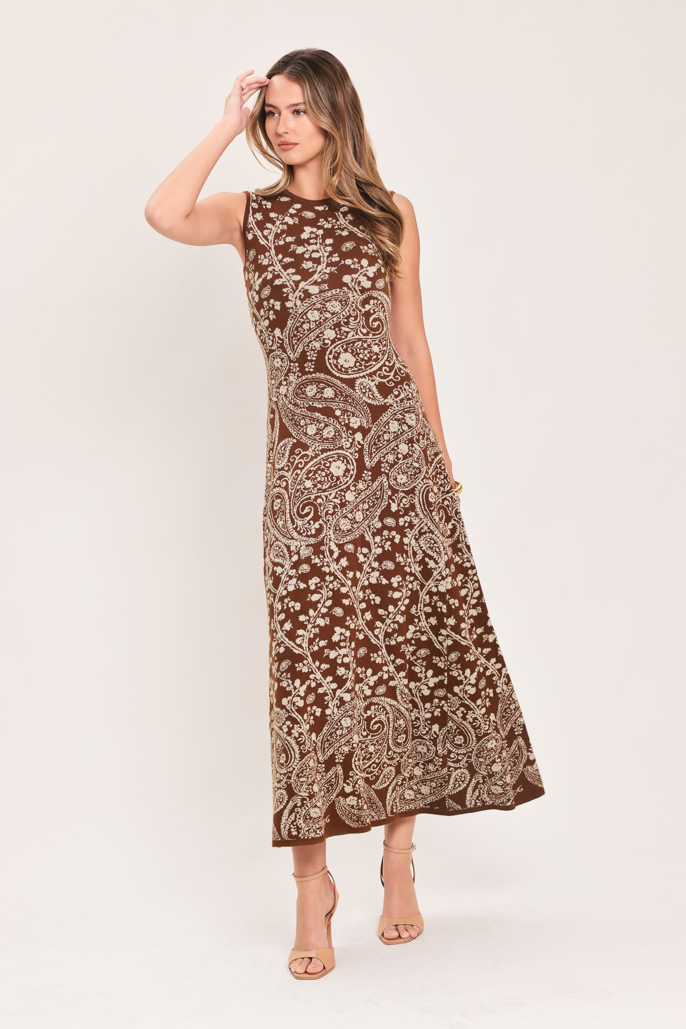 A woman wearing a sleeveless camel midi dress with an intricate white paisley and floral pattern | Flying Tomato