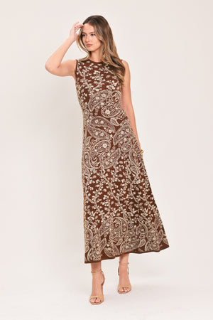 A woman wearing a sleeveless camel midi dress with an intricate white paisley and floral pattern | Flying Tomato