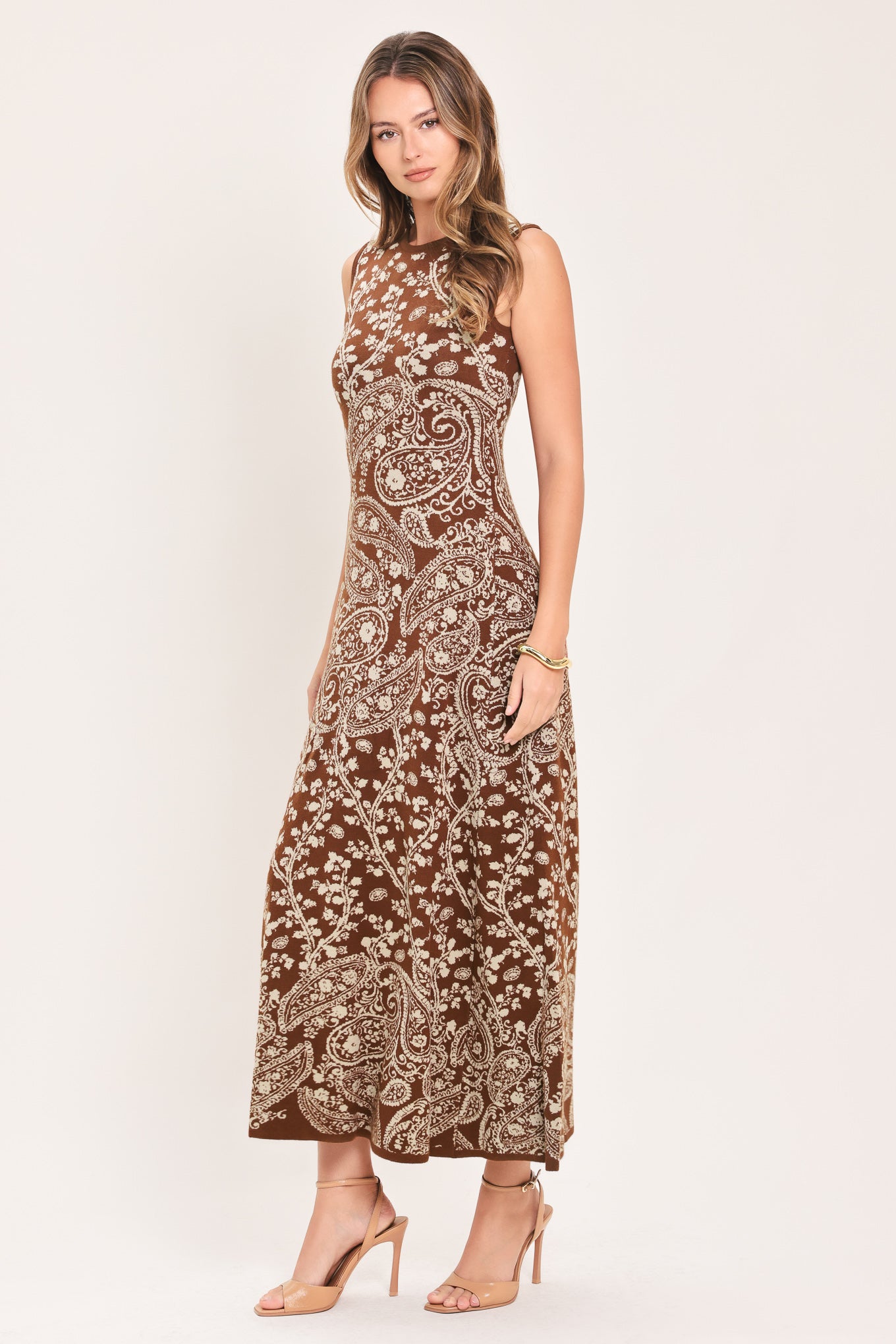 A woman wearing a sleeveless camel midi dress with an intricate white paisley and floral pattern | Flying Tomato