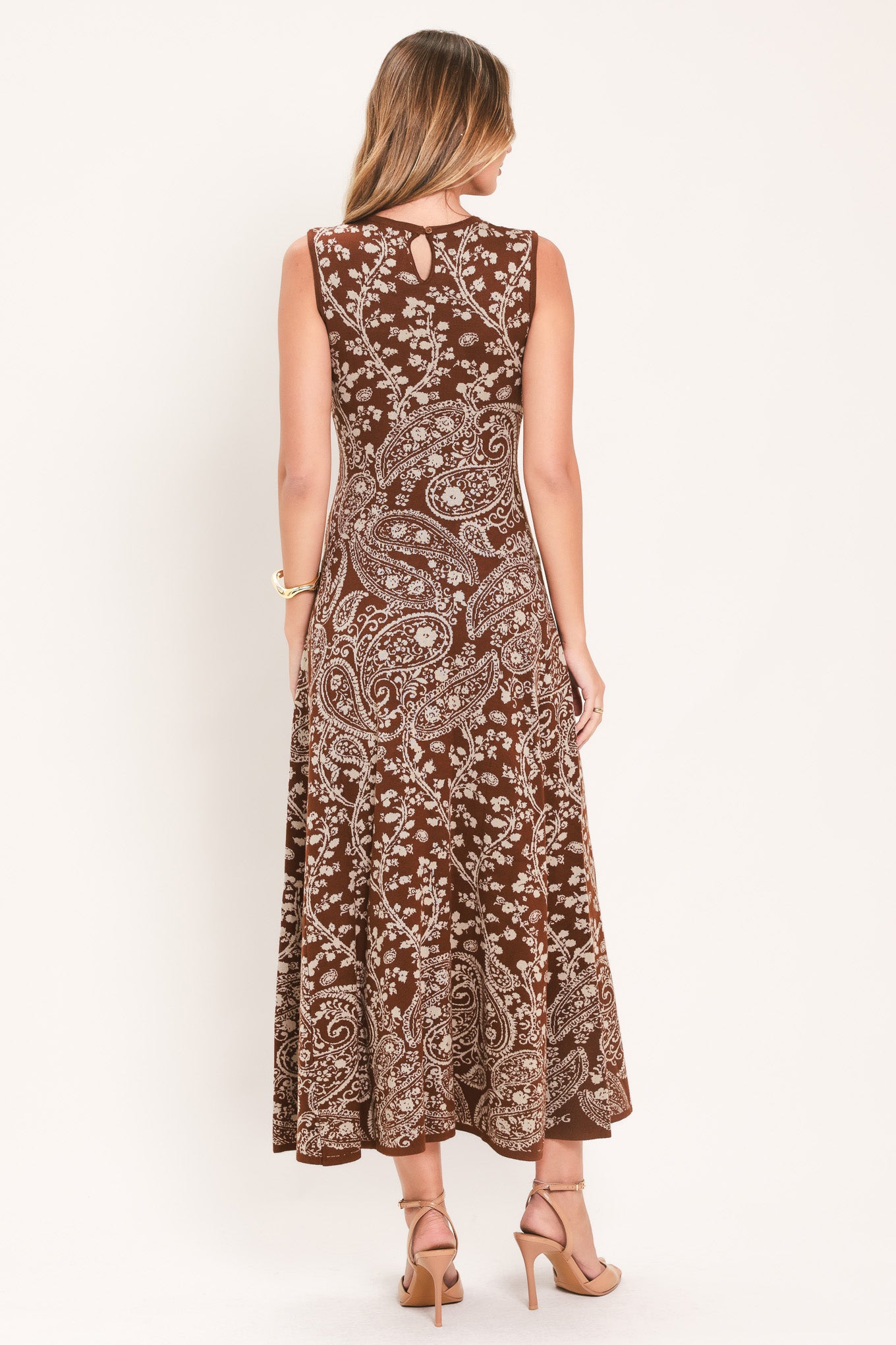 A woman wearing a sleeveless camel midi dress with an intricate white paisley and floral pattern | Flying Tomato