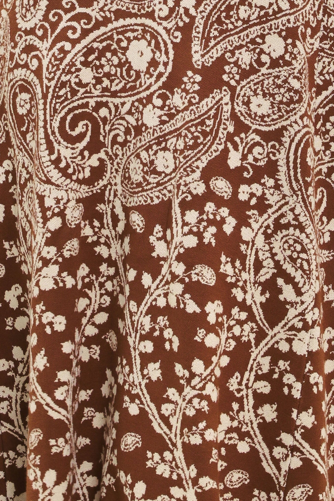 A woman wearing a sleeveless camel midi dress with an intricate white paisley and floral pattern | Flying Tomato