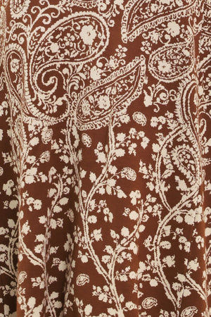 A woman wearing a sleeveless camel midi dress with an intricate white paisley and floral pattern | Flying Tomato