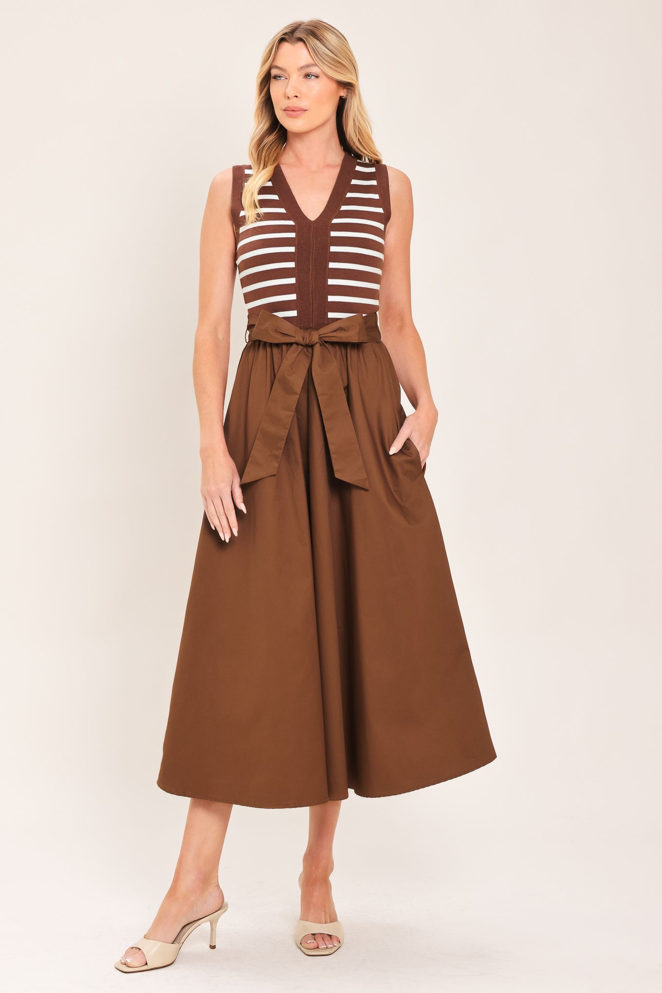 A woman wearing a sleeveless midi dress with brown and white striped top and solid brown skirt featuring a matching tie belt | Flying Tomato