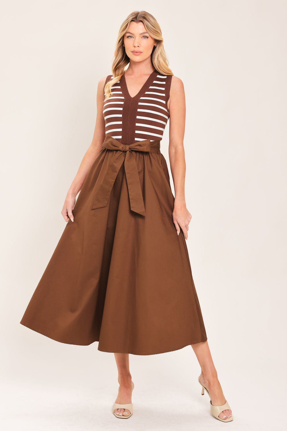A woman wearing a sleeveless midi dress with brown and white striped top and solid brown skirt featuring a matching tie belt | Flying Tomato