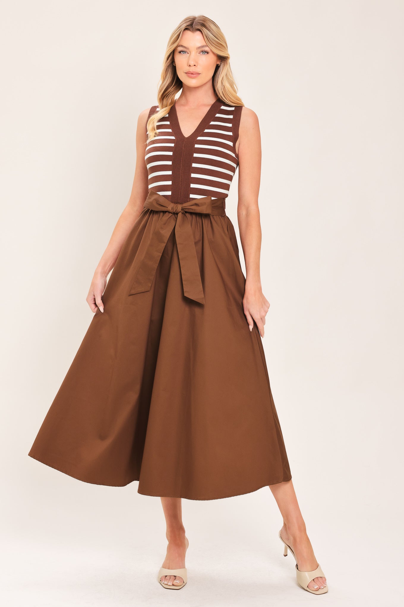 A woman wearing a sleeveless midi dress with brown and white striped top and solid brown skirt featuring a matching tie belt | Flying Tomato