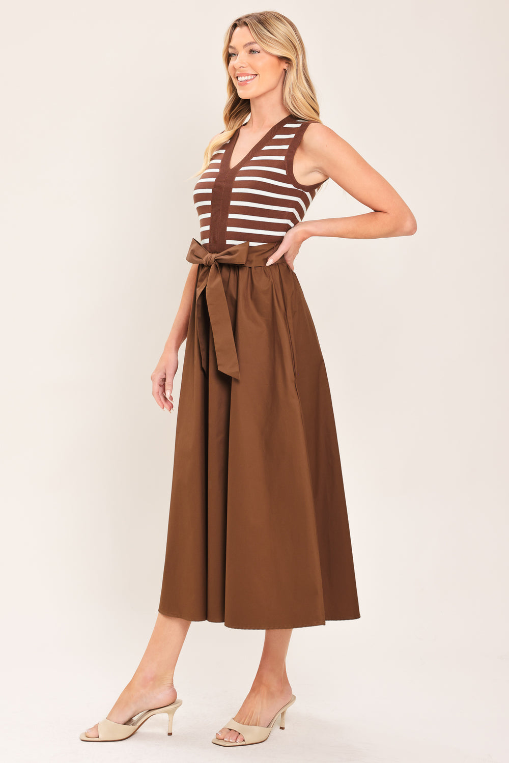 A woman wearing a sleeveless midi dress with brown and white striped top and solid brown skirt featuring a matching tie belt | Flying Tomato