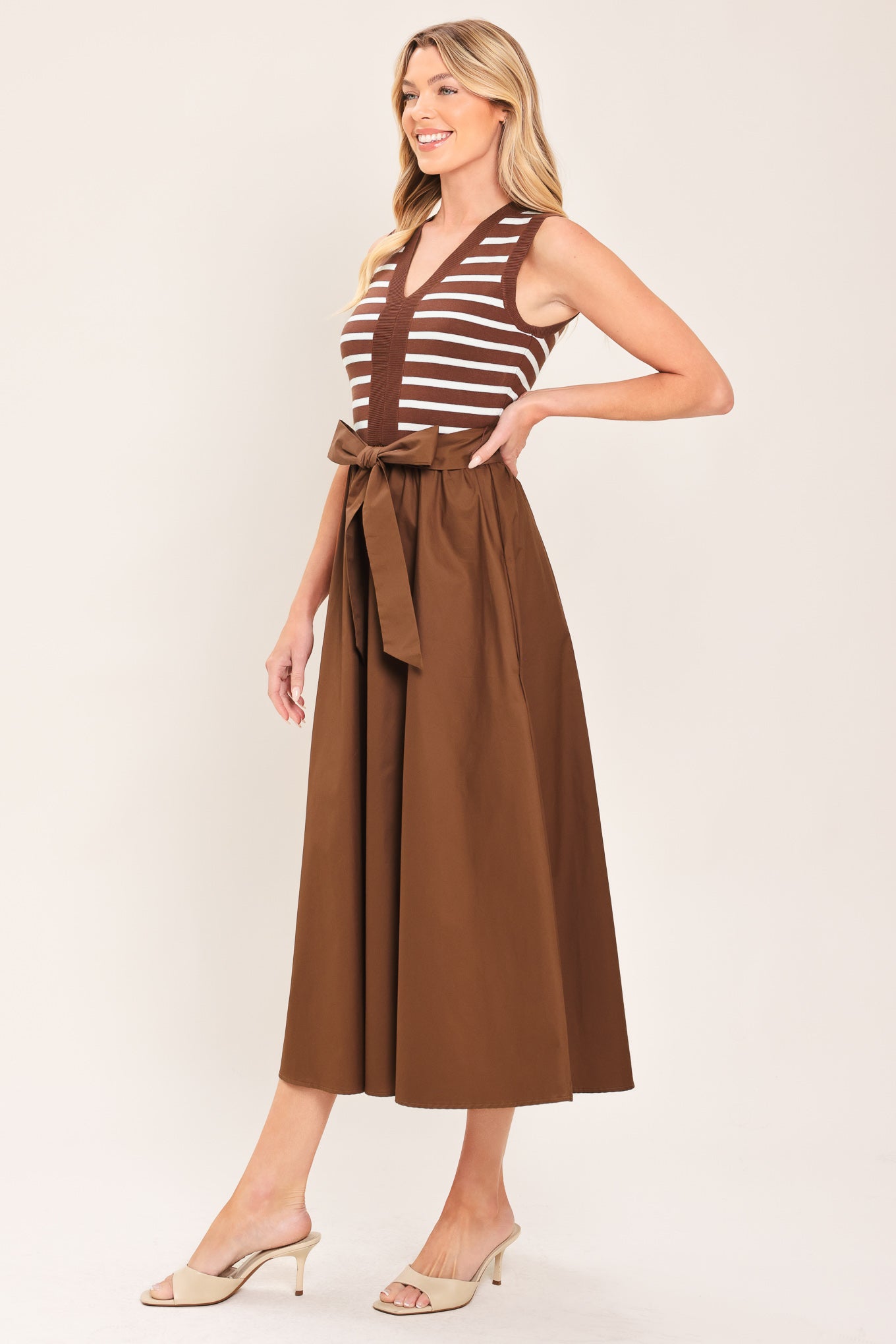 A woman wearing a sleeveless midi dress with brown and white striped top and solid brown skirt featuring a matching tie belt | Flying Tomato