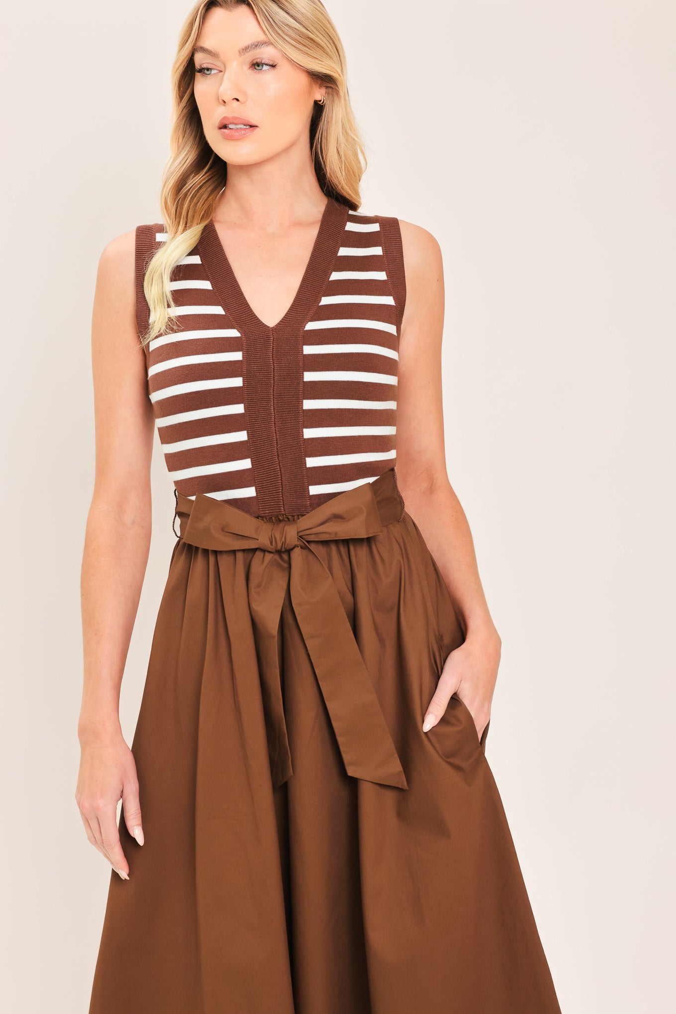A woman wearing a sleeveless midi dress with brown and white striped top and solid brown skirt featuring a matching tie belt | Flying Tomato