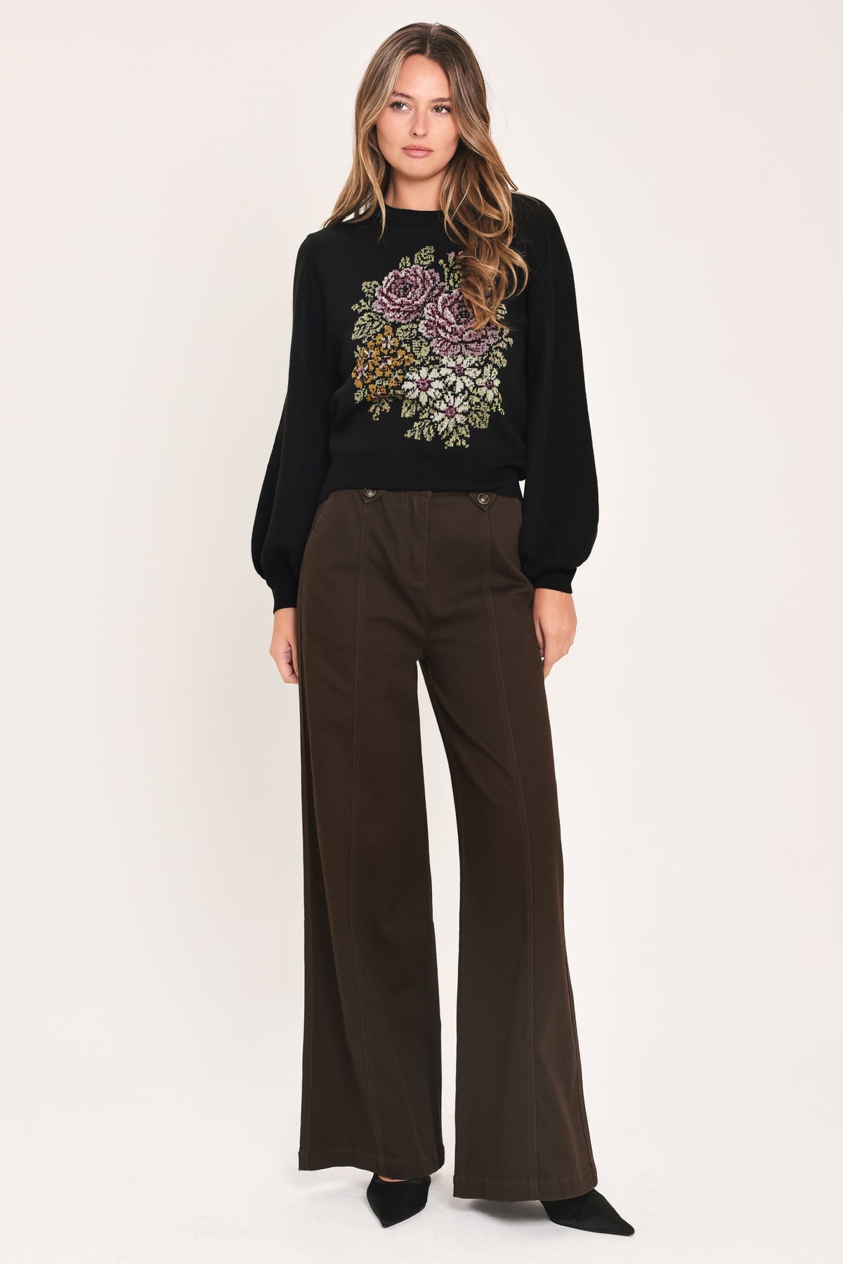 A woman modeling a black crewneck sweatshirt featuring a large embroidered floral design in purple, green, and gold on the front | Flying Tomato