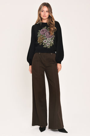 A woman modeling a black crewneck sweatshirt featuring a large embroidered floral design in purple, green, and gold on the front | Flying Tomato