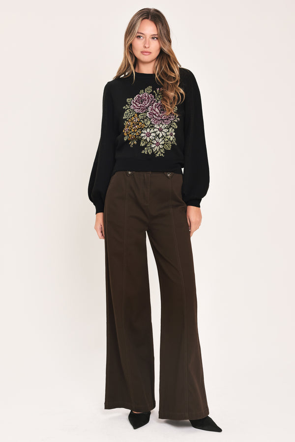 A woman modeling a black crewneck sweatshirt featuring a large embroidered floral design in purple, green, and gold on the front | Flying Tomato
