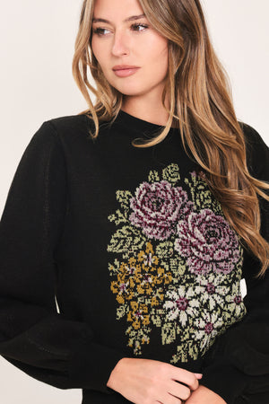 A woman modeling a black crewneck sweatshirt featuring a large embroidered floral design in purple, green, and gold on the front | Flying Tomato