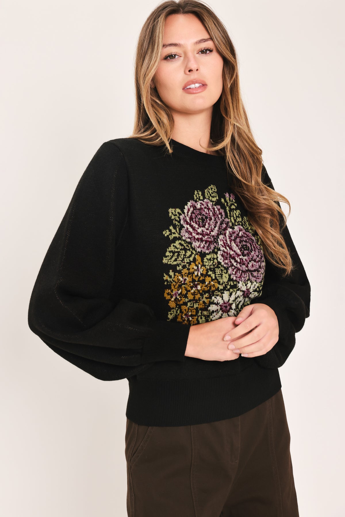 A woman modeling a black crewneck sweatshirt featuring a large embroidered floral design in purple, green, and gold on the front | Flying Tomato