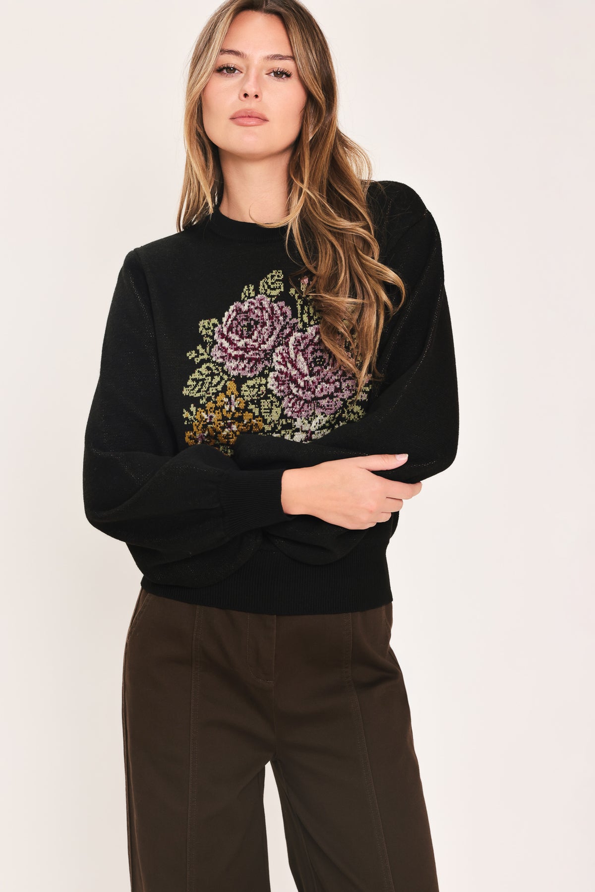 A woman modeling a black crewneck sweatshirt featuring a large embroidered floral design in purple, green, and gold on the front | Flying Tomato