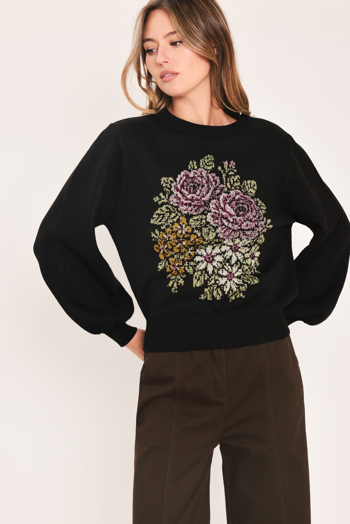A woman modeling a black crewneck sweatshirt featuring a large embroidered floral design in purple, green, and gold on the front | Flying Tomato
